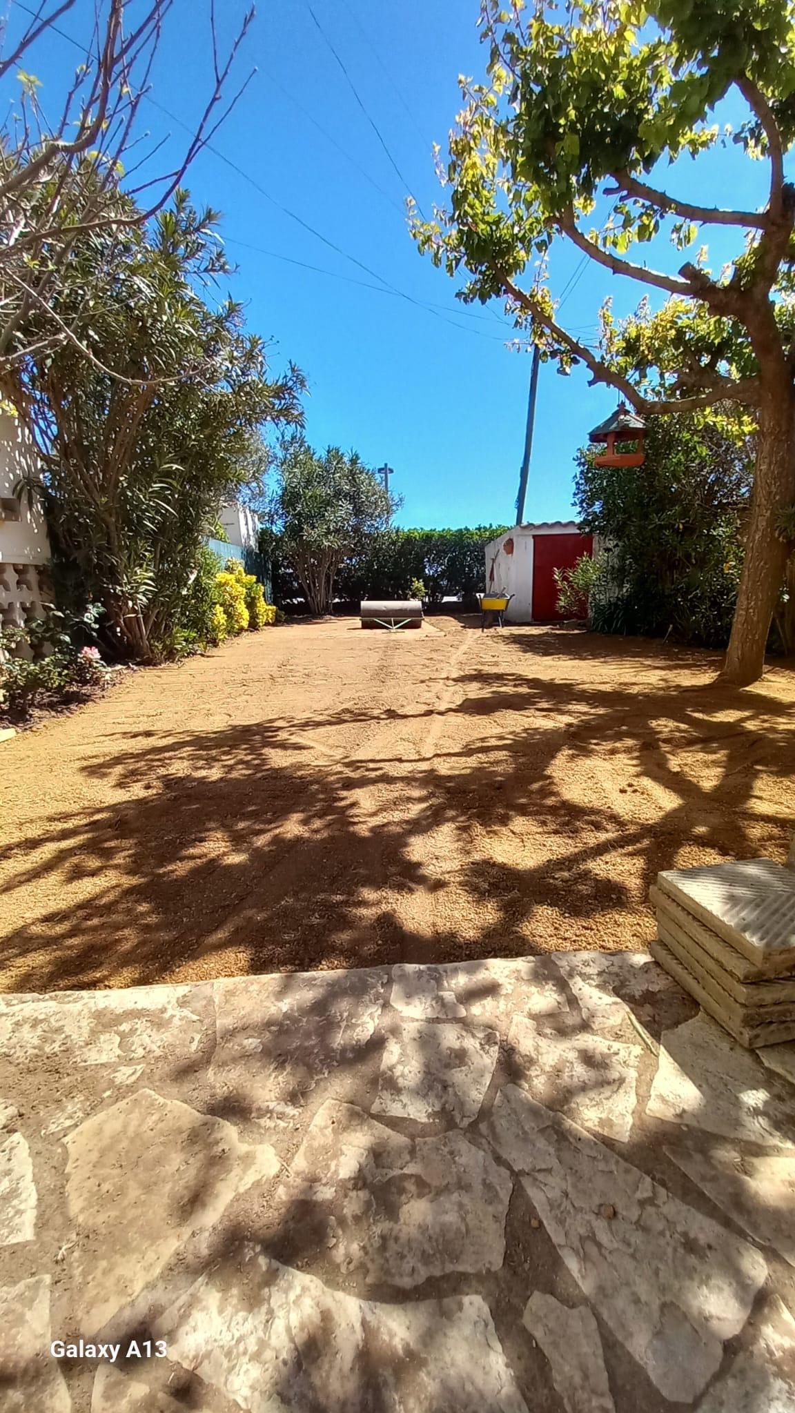 Terreno del jardín rastrillado y nivelado, con el rodillo compactador apoyado al fondo