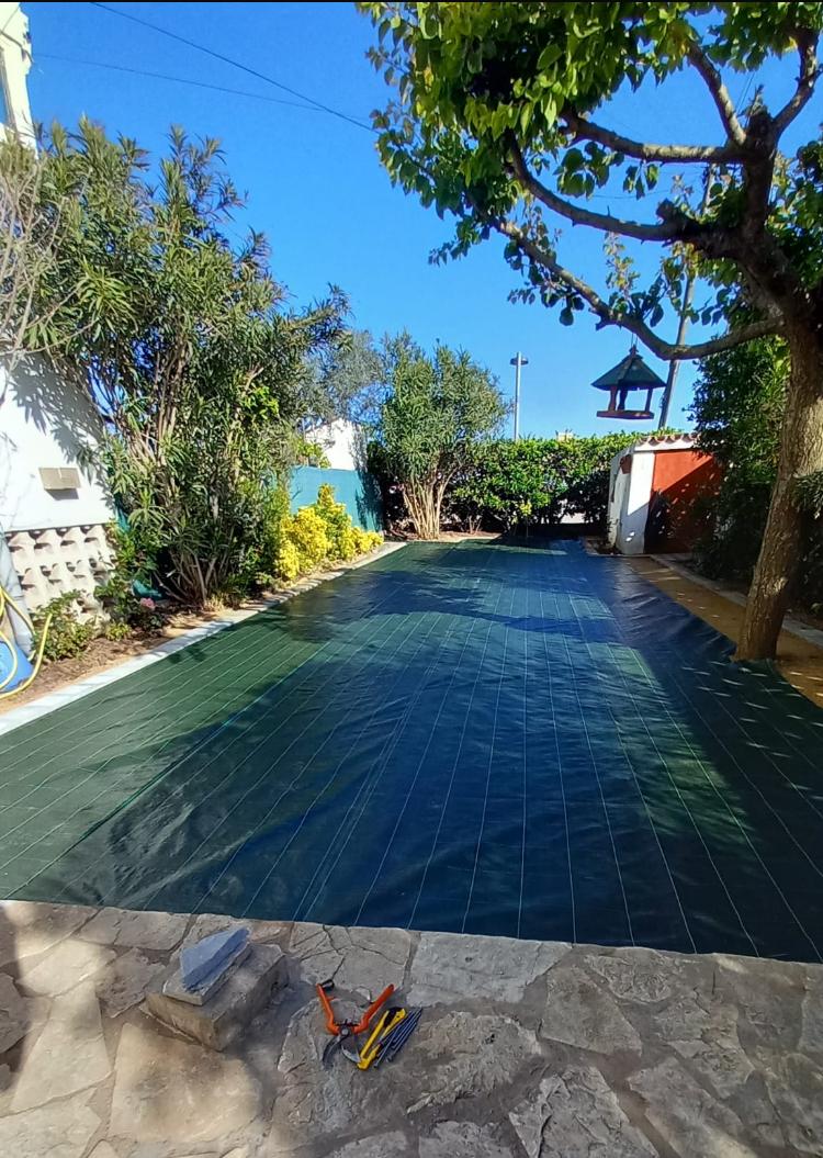Malla antihierbas verde extendida y grapada sobre el terreno ya compactado del jardín